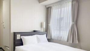 Une chambre d’hôtel avec un lit, une table de chevet, une lampe et une fenêtre avec des rideaux.