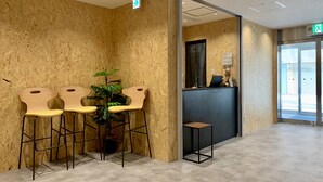 Un espace d’accueil avec un mur en bois, deux chaises en bois, une petite table, une plante en pot et un comptoir de réception.