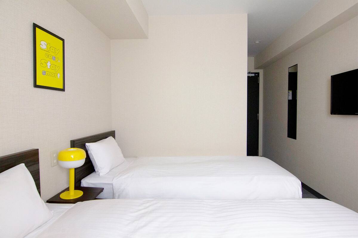 A hotel room with two beds, a yellow lamp, and a framed motivational poster on the wall.