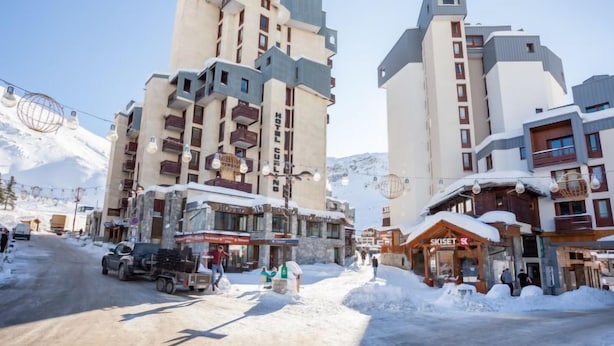 Ein Hotel mit mehreren Etagen, ein Sessellift im Hintergrund und eine verschneite Straße.