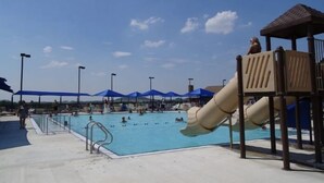 Ein Schwimmbeckenbereich mit Rutsche, Sonnenschirmen und einer überdachten Sitzgelegenheit.
