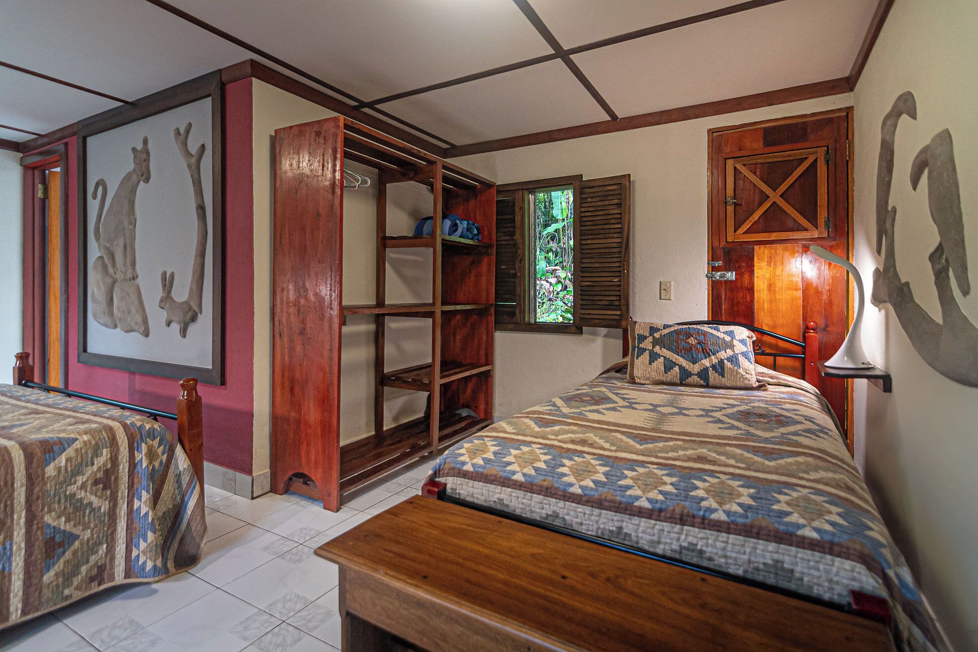 A room with two beds, a wooden wardrobe, a window with shutters, and a wall-mounted lamp.