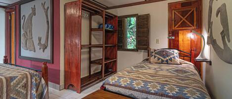 A room with two beds, a wooden wardrobe, a window with shutters, and a wall-mounted lamp.