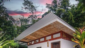 A small, single-story house with a sloped roof, surrounded by lush greenery and flowering plants. - Talamanca Nature Reserve (Rivas)
