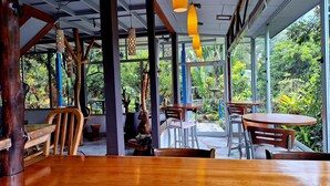 A restaurant with wooden tables and chairs, large windows, and hanging pendant lights. - Talamanca Nature Reserve (Rivas)