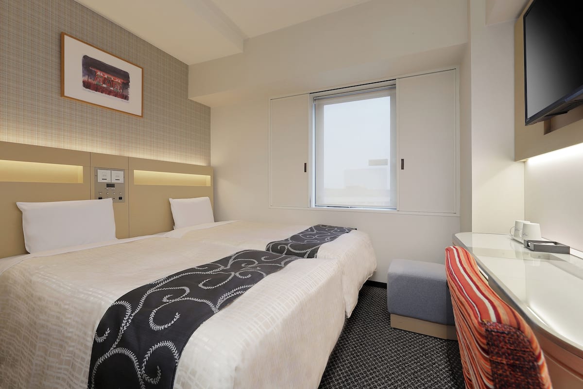 A hotel room with a large bed, a bedside table, a TV, and a window.