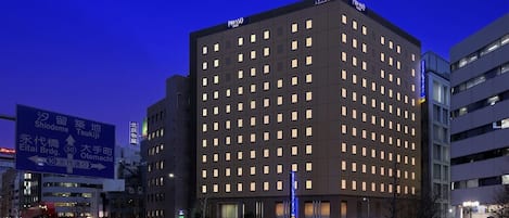 A modern hotel with a grid of windows, signage indicating nearby locations, and a well-lit entrance.