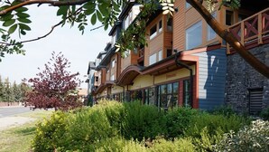 A row of modern buildings with a mix of wood and stone facades, a well-maintained garden, and a clear sky. - Amazing Rocky Mountain Views: Spacious, Bright, Comfortable Condo, Free WIFI (Canmore)