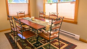 A dining room with a wooden table, six chairs, a chandelier, and large windows with mountain views. - Amazing Rocky Mountain Views: Spacious, Bright, Comfortable Condo, Free WIFI (Canmore)