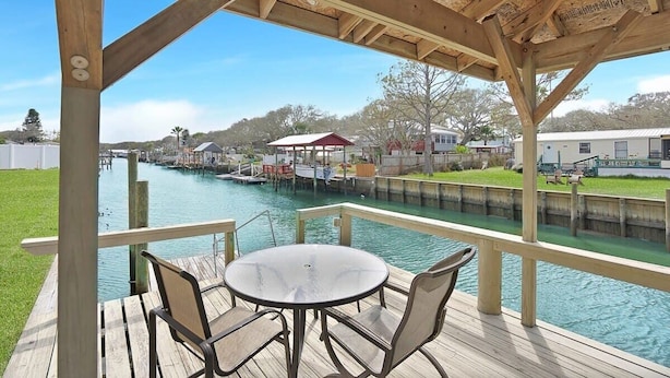 A wooden deck with a table and chairs overlooking a canal with boats and houses in the background. - On the Canal, by Beach, Kayaks, Dock, Fishing (St. Augustine)