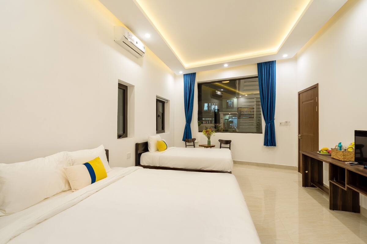 A hotel room with two beds, a desk, a TV, and a window with curtains.