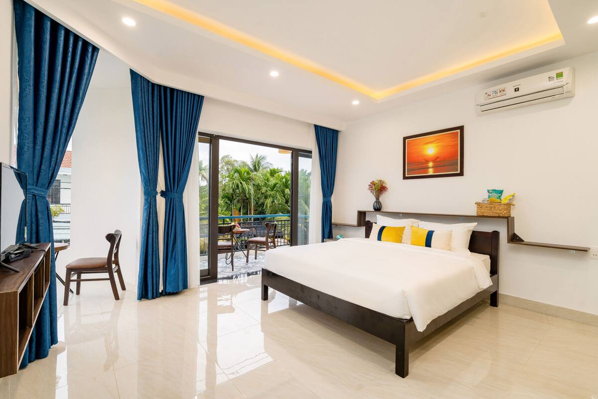 A modern hotel room with a large bed, a desk, and a balcony with a view of palm trees.