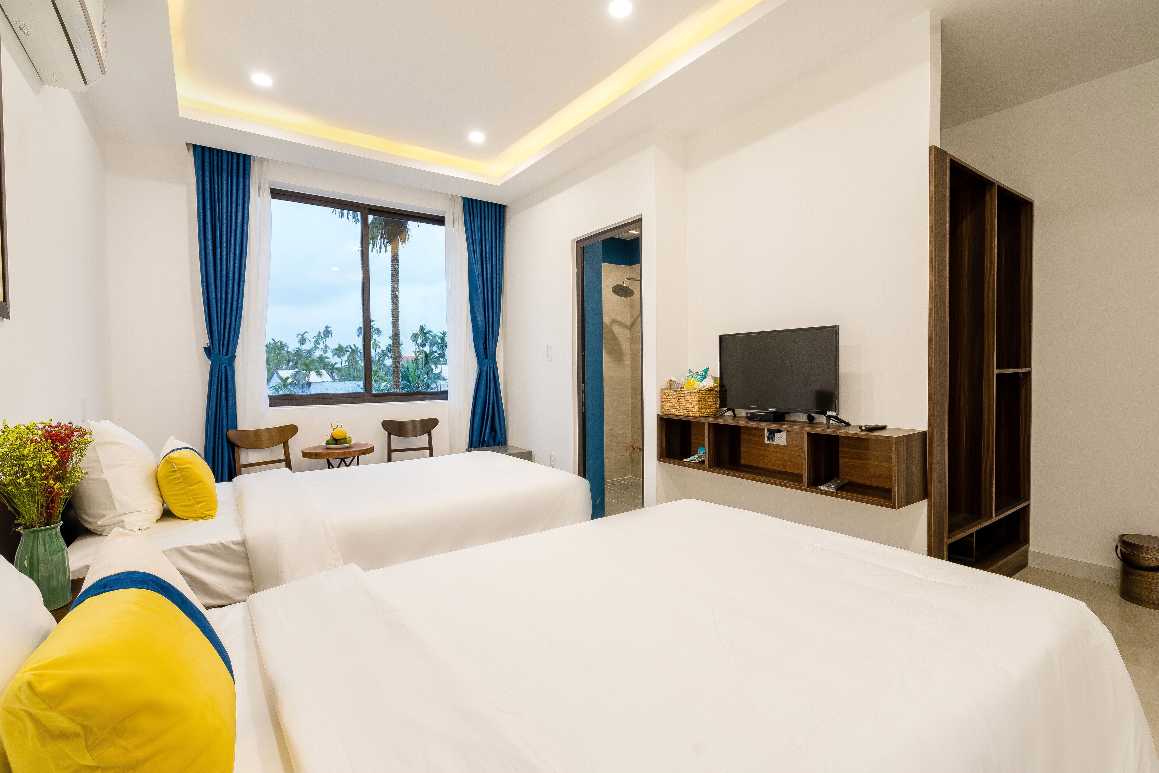 Habitación de hotel con dos camas, un televisor, una mesita con una cesta y un armario.
