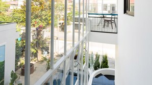 A modern interior with a staircase leading to a balcony with a glass railing, offering a view of the street and greenery below. - 5 Coconut Homestay Hoi An (Da Nang)