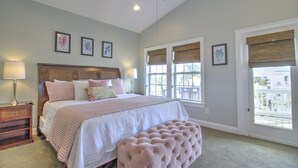 A bedroom with a bed, bedside tables, a bench, and large windows with blinds.