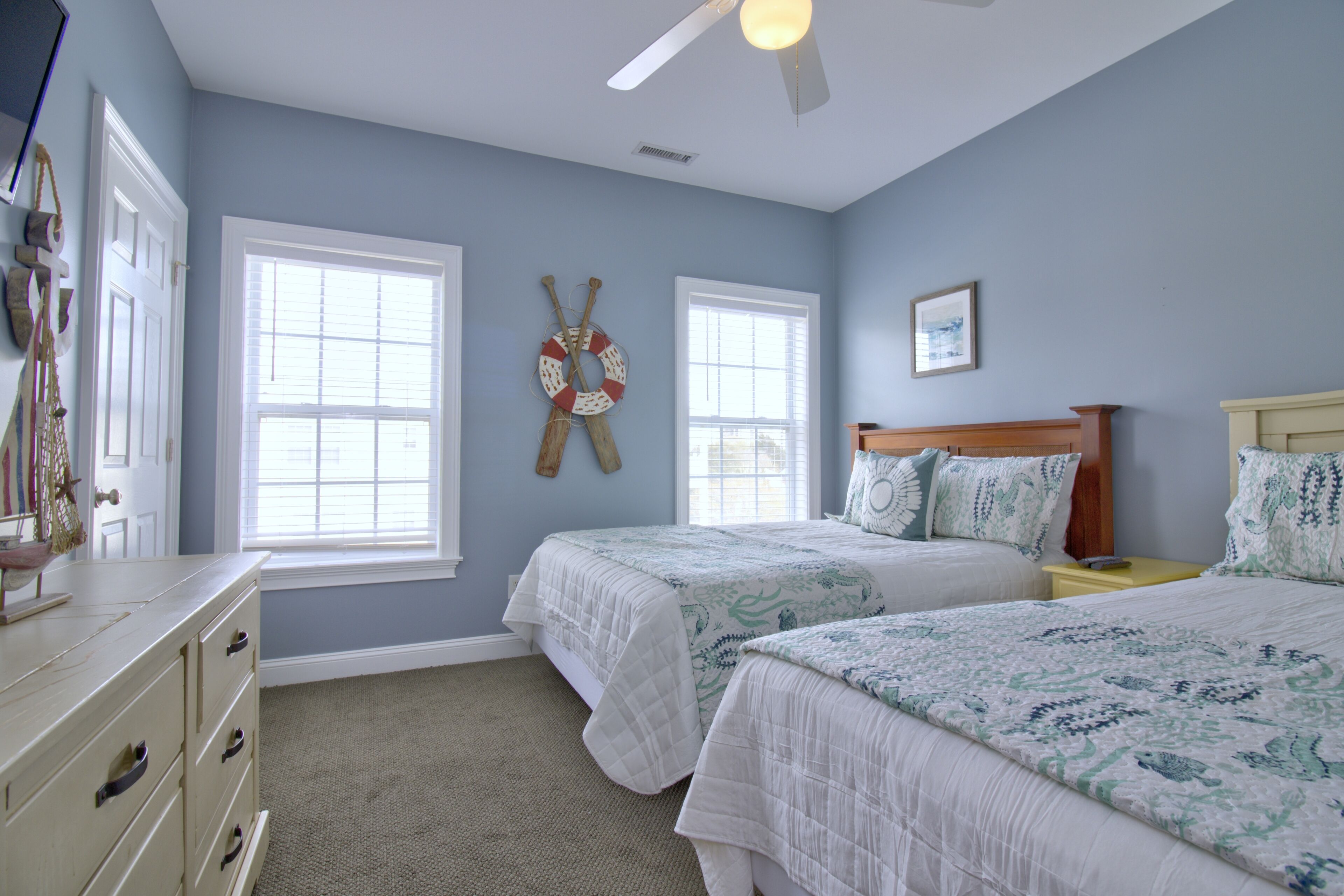 A bedroom with two beds, a dresser, a ceiling fan, and two windows.