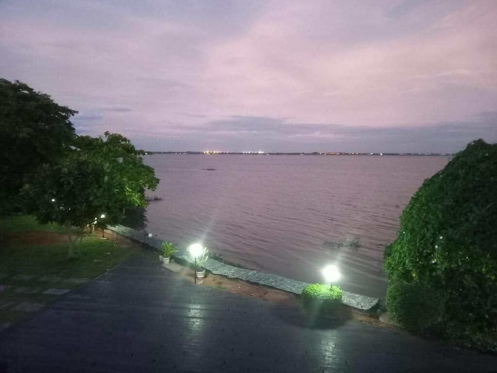 A waterfront view with a paved walkway, street lamps, and a distant cityscape.