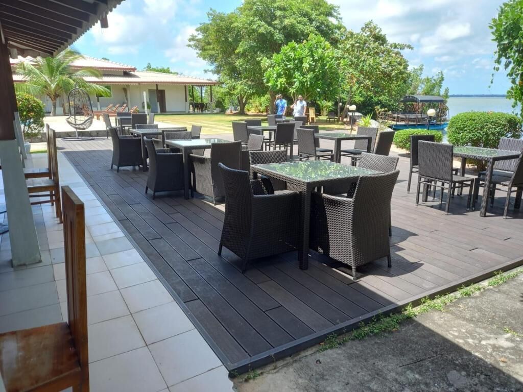 Área de pátio externa com mesas e cadeiras, piscina e vista para o mar.