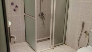 A bathroom with a glass-enclosed shower, a toilet, and a brown bath mat.
