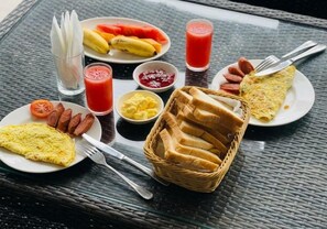 A breakfast table with various food items, including toast, sausages, eggs, and a fruit plate. - Nilakma Lagoon (Negombo)