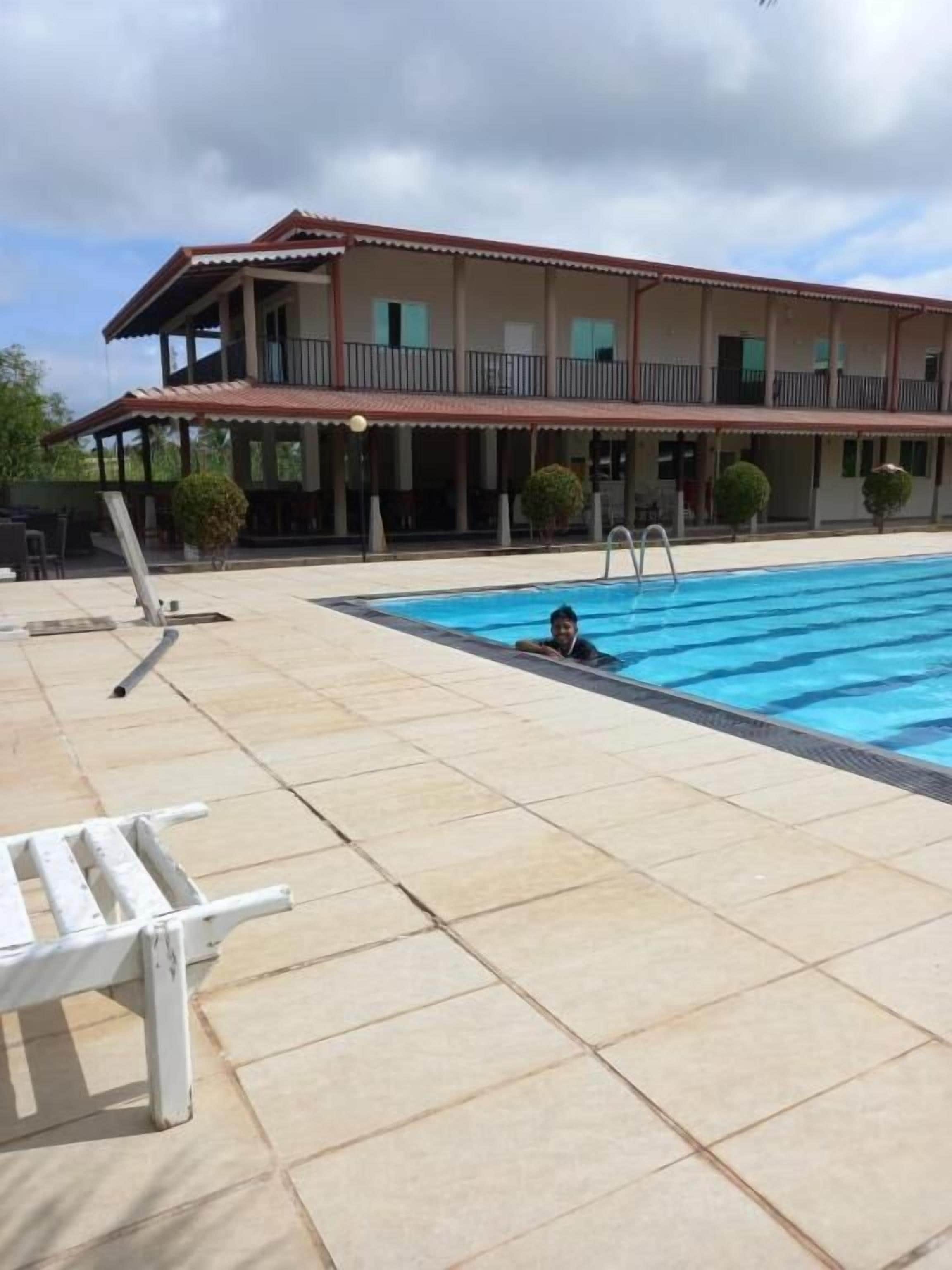 Zona de piscina con una escalera, un banco blanco y un edificio con balcón al fondo.