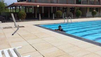 Zona de piscina con una escalera, un banco blanco y un edificio con balcón al fondo.