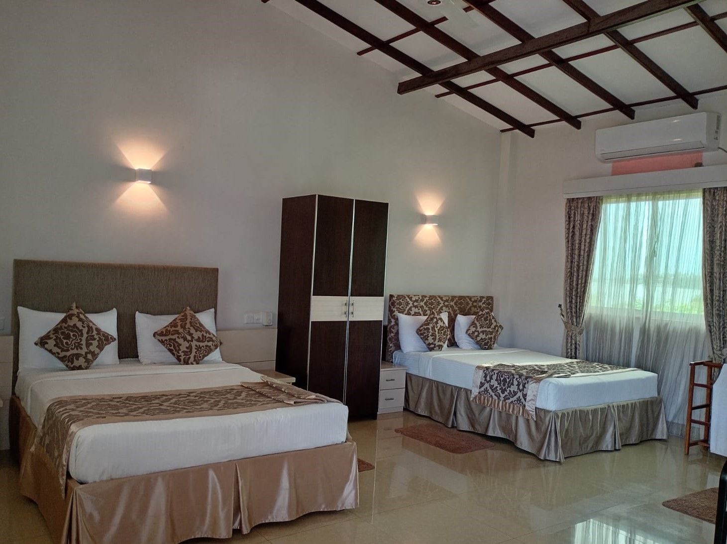 A hotel room with two beds, a wardrobe, a ceiling fan, and an air conditioning unit.