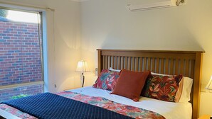 A neatly made bed with a floral bedspread, a wooden headboard, and a nightstand with a lamp. - Maroondah 3 Bedroom House (Kilsyth)