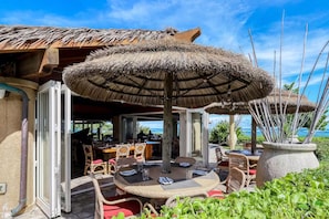 Enjoy al fresco dining with ocean views under a shaded area surrounded by lush greenery.