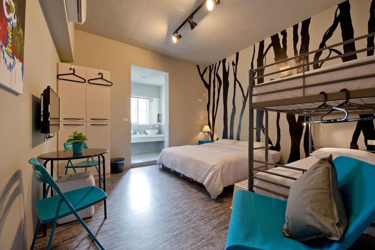 Une chambre d’hôtel compacte avec un lit superposé, une petite table avec des chaises, un téléviseur et une salle de bain visible à travers une porte ouverte.