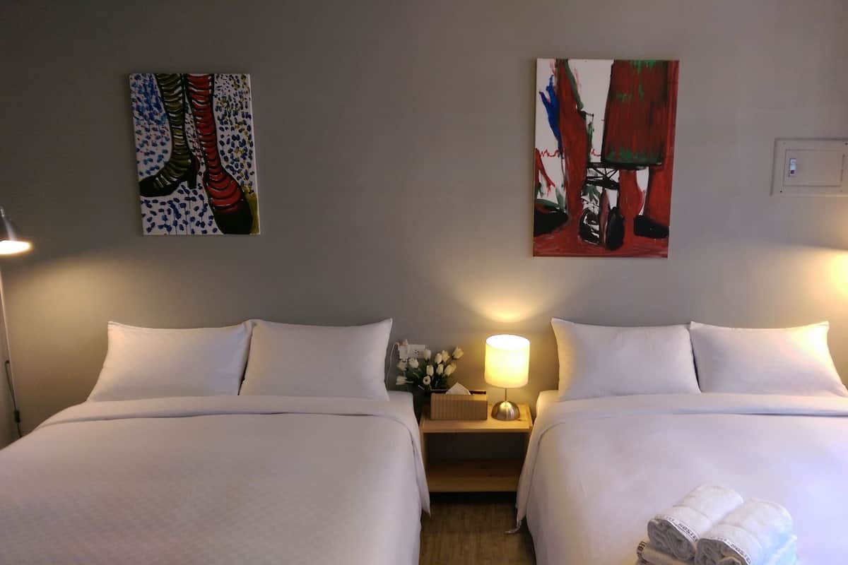 Une chambre d’hôtel avec deux lits, une table de chevet avec une lampe et deux tableaux au mur.