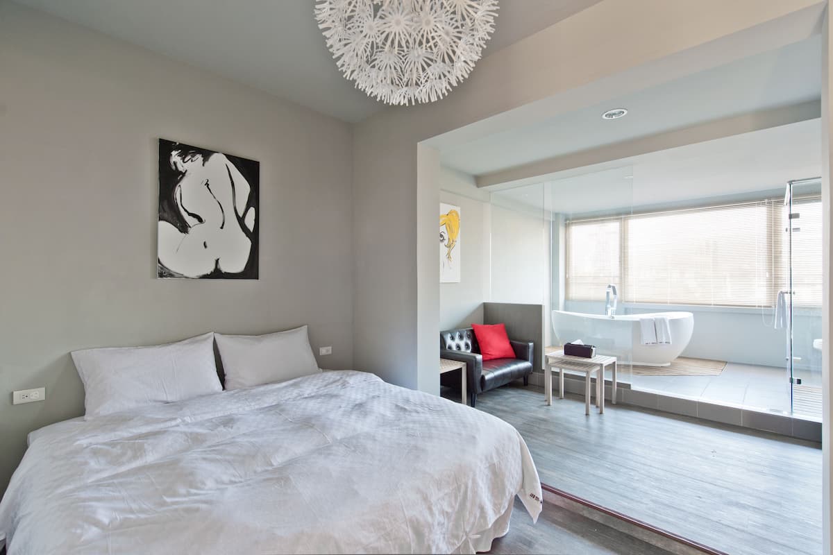 Une chambre moderne avec un grand lit, un canapé, une petite table et une salle de bain équipée d’une baignoire et d’une douche.