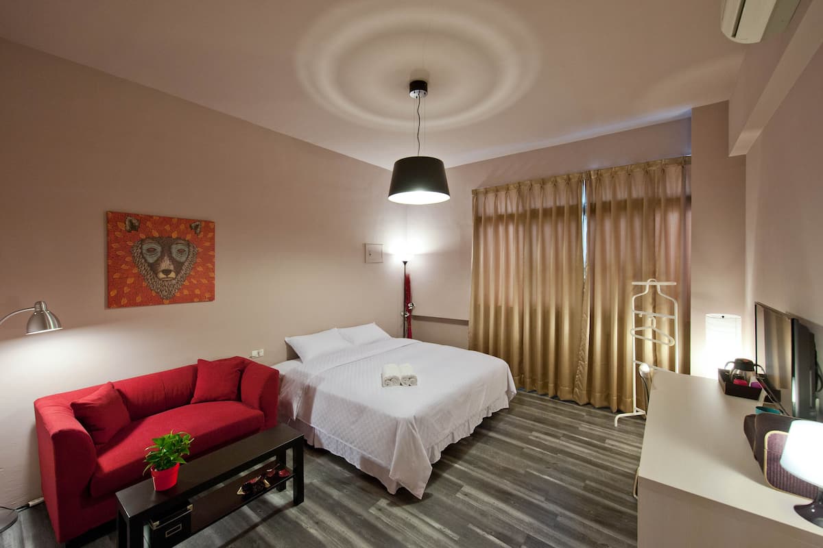 Une chambre d’hôtel avec un lit, un canapé rouge, un bureau, une télévision et une fenêtre avec des rideaux.