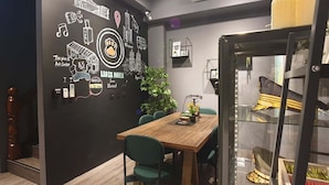 A dining area with a wooden table and chairs, a black wall with various doodles and text, and a glass partition with items on display. - Leo 111 - Yancheng Pier 2 (Kaohsiung)