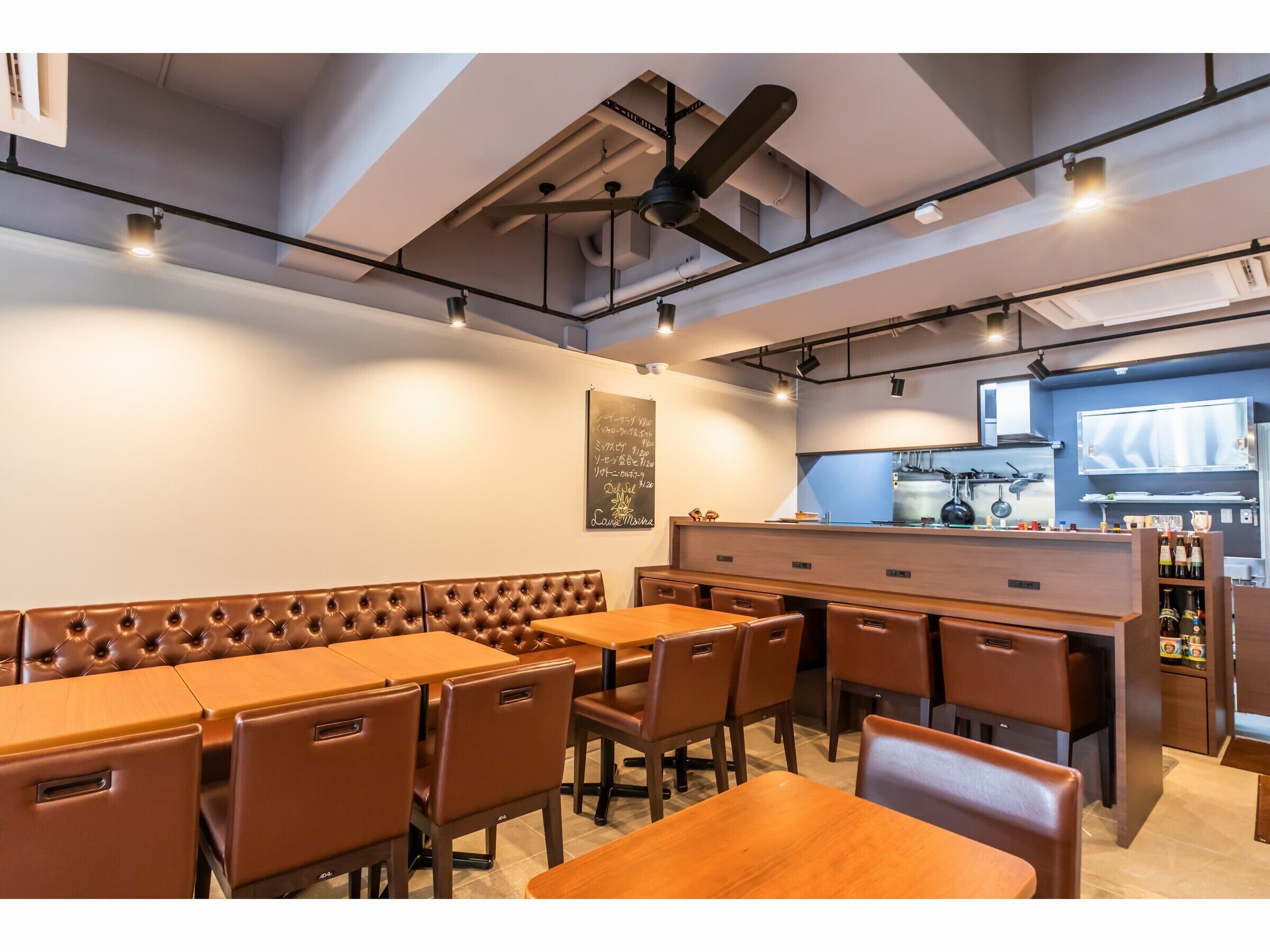 Ein Restaurant mit einer langen Sitzbank, mehreren Tischen und einer im Hintergrund sichtbaren Küche.