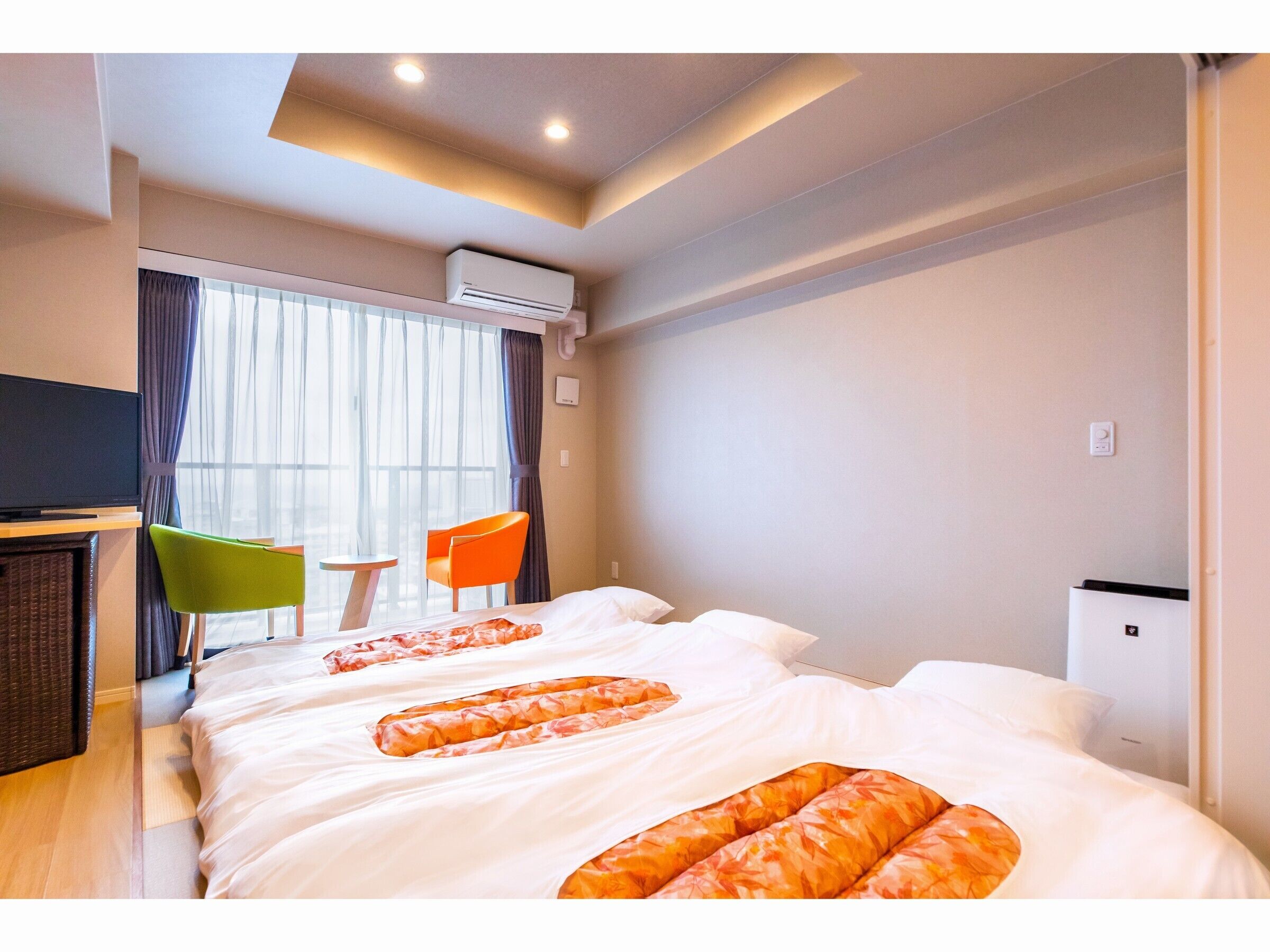 Una habitación de hotel con cama, escritorio, dos sillas, aire acondicionado y ventana con cortinas.