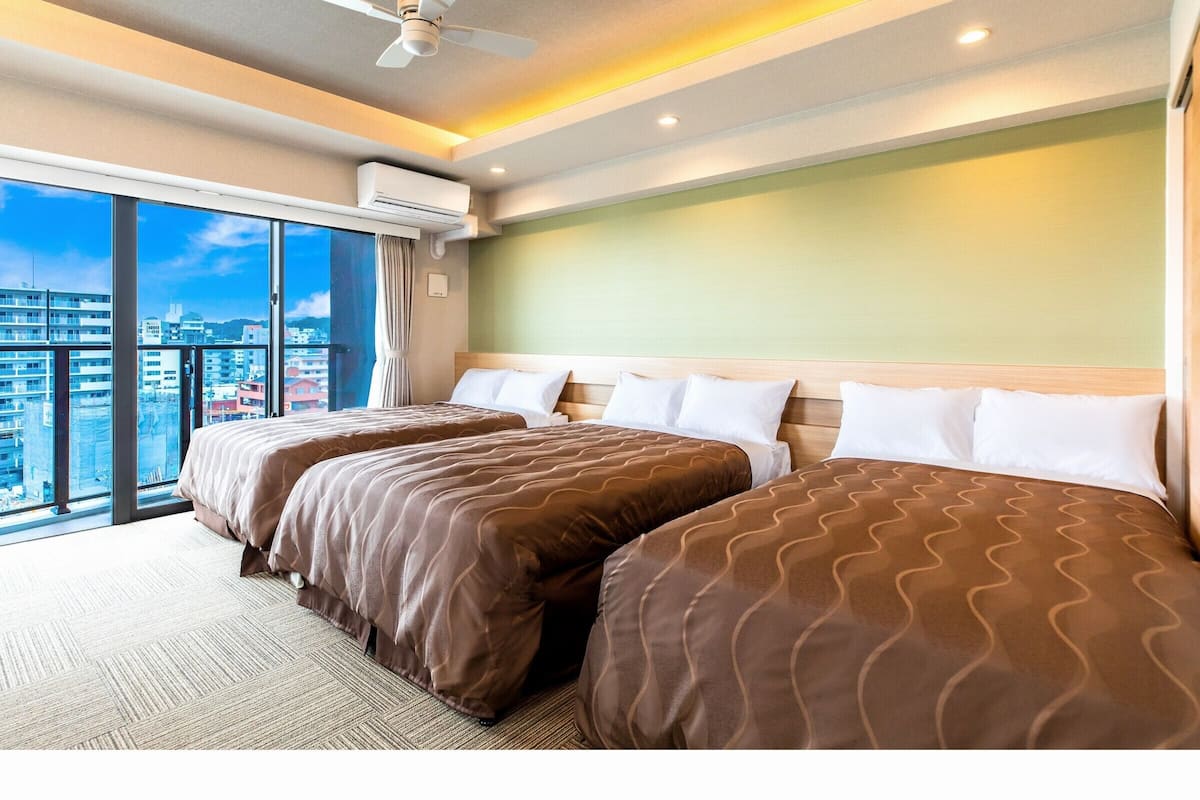 Habitación de hotel con dos camas, ventilador de techo y un amplio ventanal con vistas a la ciudad.