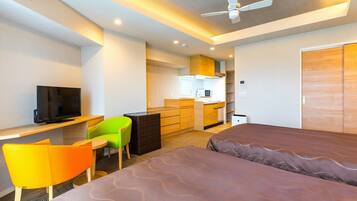 Habitación de hotel con cama, escritorio con televisor, silla, kitchenette y armario.