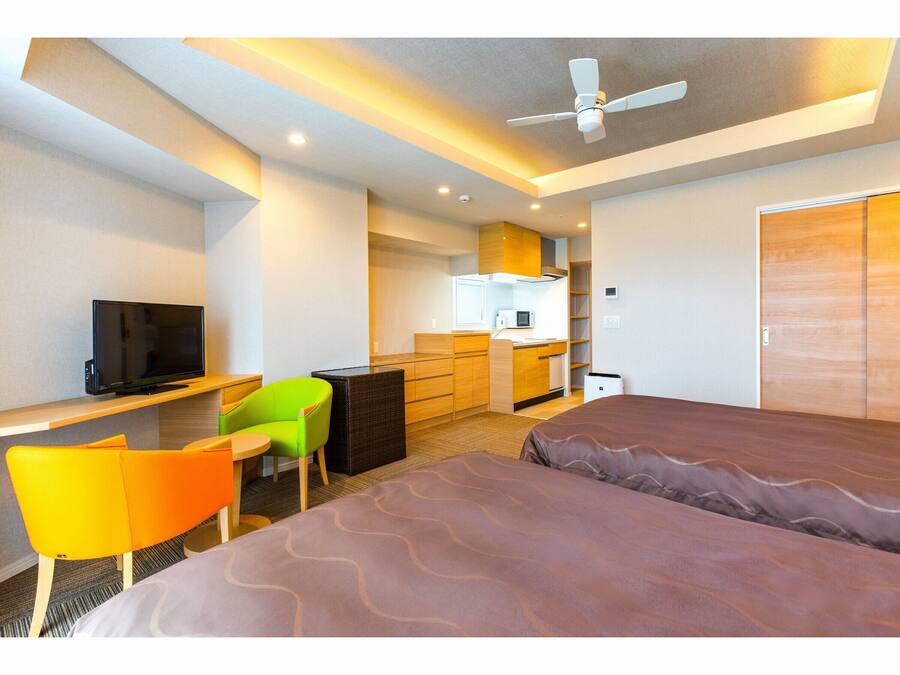 Habitación de hotel con cama, escritorio con televisor, silla, kitchenette y armario.