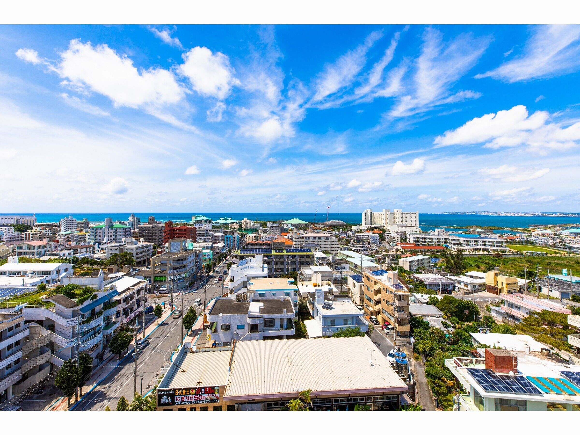 A coastal cityscape with a mix of residential and commercial buildings, a clear blue sky, and a view of the ocean.