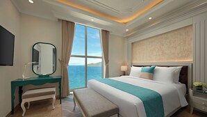 Une chambre d’hôtel avec un grand lit, un bureau avec une chaise, une table de chevet et une vue sur la mer.