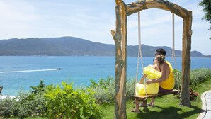 A person sitting on a swing with a view of the sea and mountains.