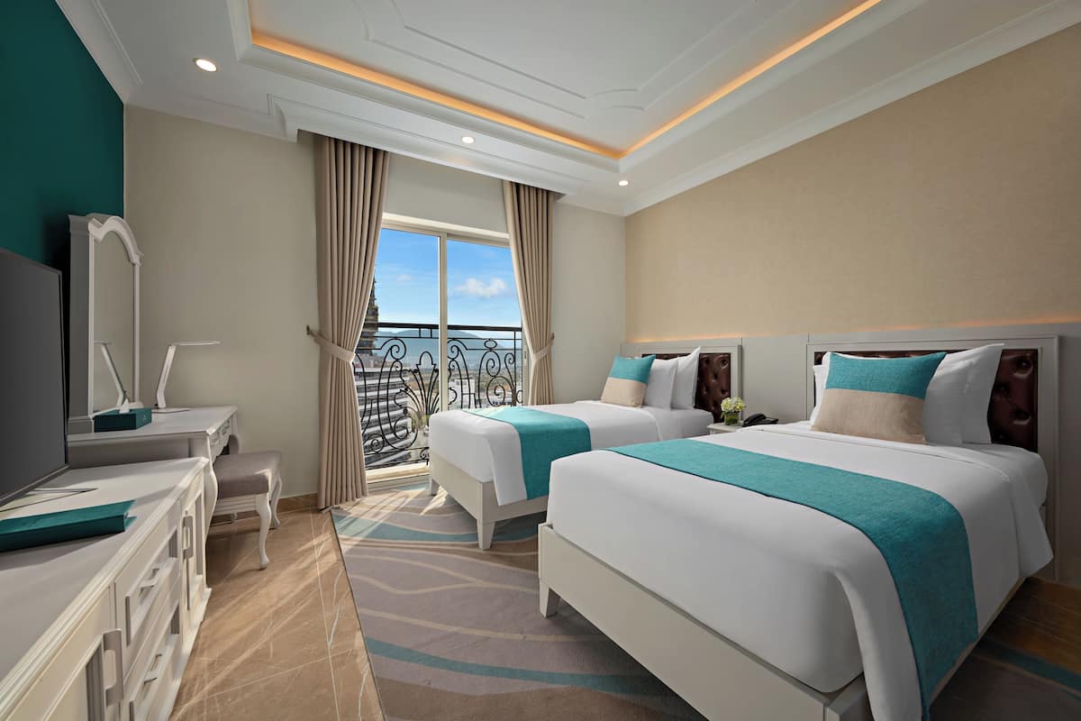 A hotel room with two beds, a desk, a chair, a TV, and a balcony with a view.