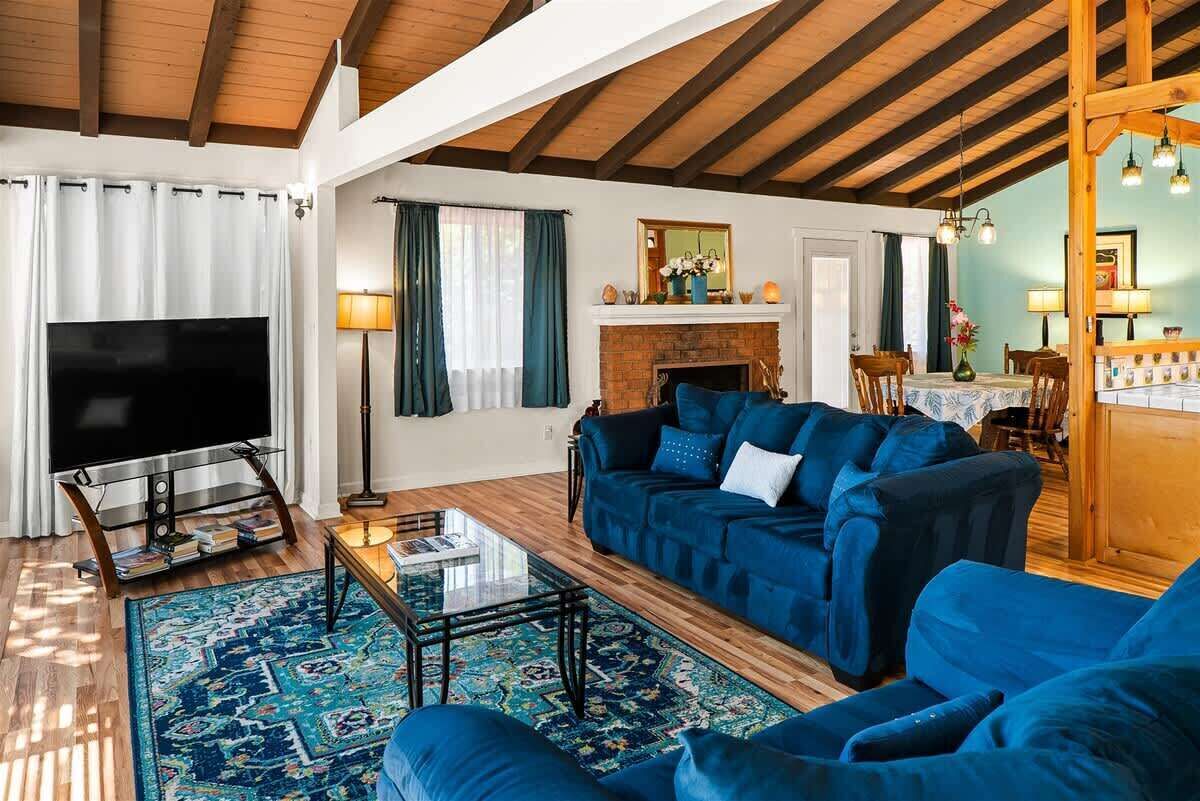 Een woonkamer met een televisie, een blauwe bank, een open haard en houten balken.
