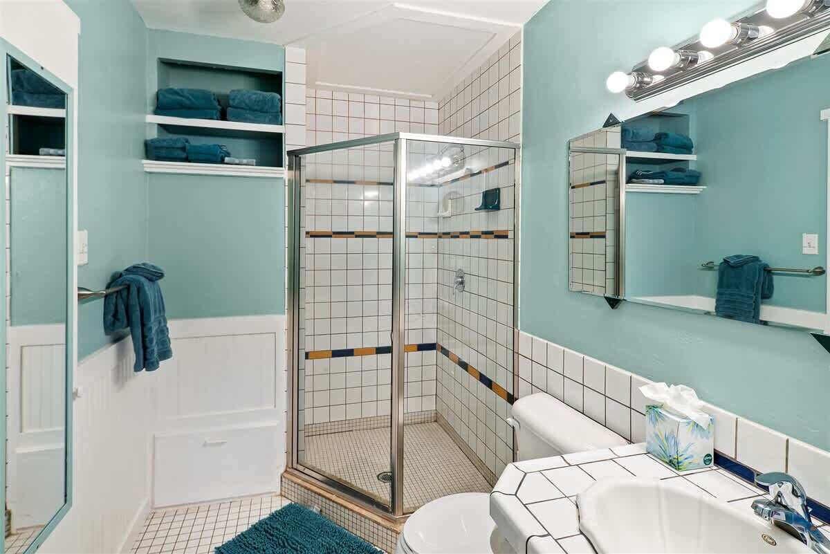 A bathroom with a shower, toilet, sink, and shelves with towels.