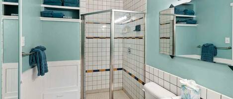 A bathroom with a shower, toilet, sink, and shelves with towels.
