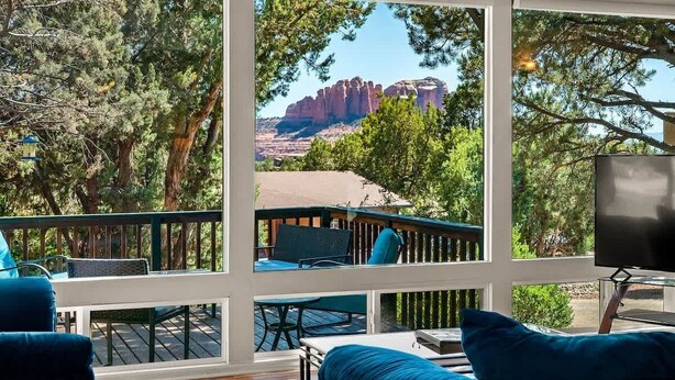 Una habitación con ventanas amplias, una terraza y vistas a formaciones rocosas rojas.