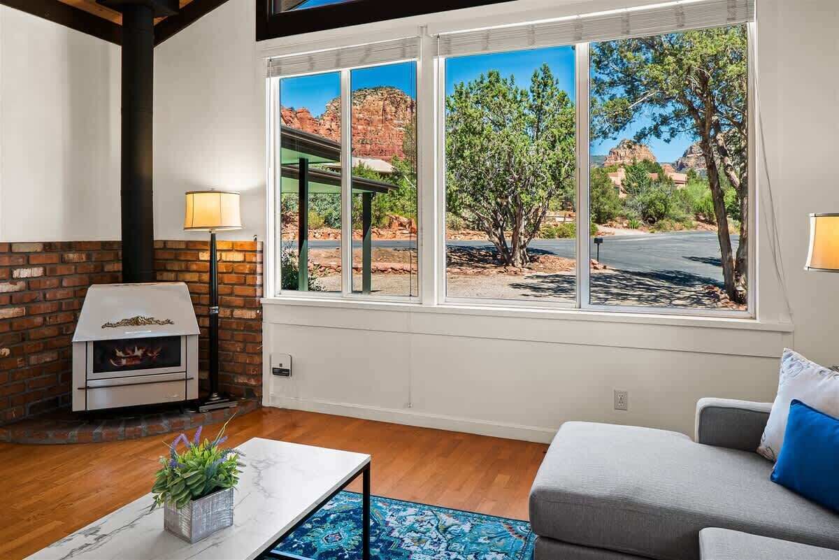 A living room with a fireplace, a sofa, a coffee table, and a large window with a view of red rock formations.