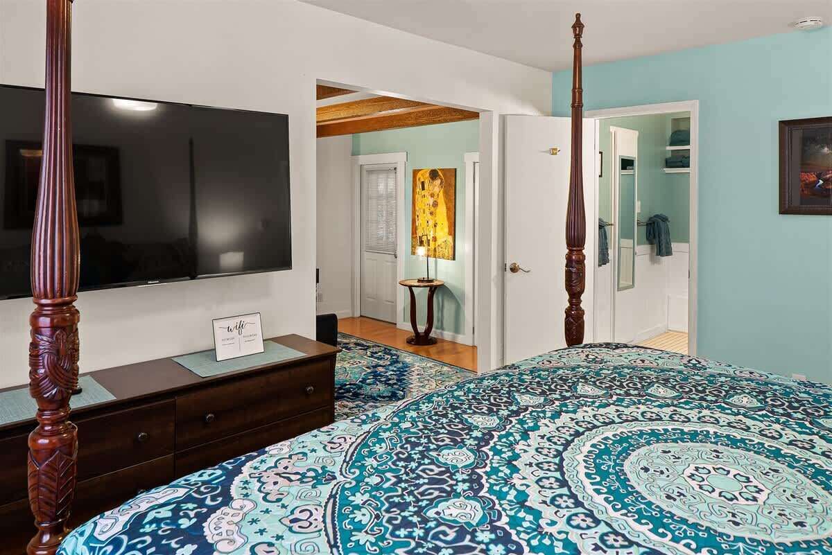 A bedroom with a four-poster bed, a flat-screen TV, a dresser, and a door leading to a bathroom.