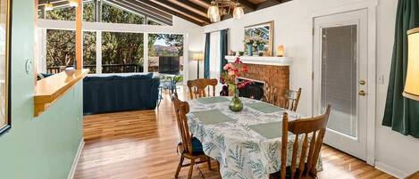 A dining area with a table set for four, wooden chairs, a fireplace, and a view of the outdoors.